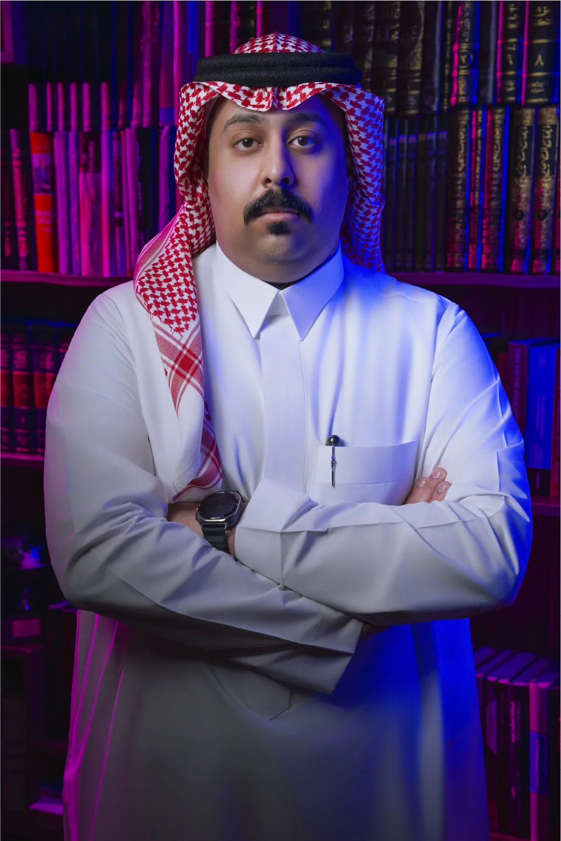 Portrait of a smiling man wearing a traditional Middle Eastern white thobe and checkered keffiyeh against a purple background.