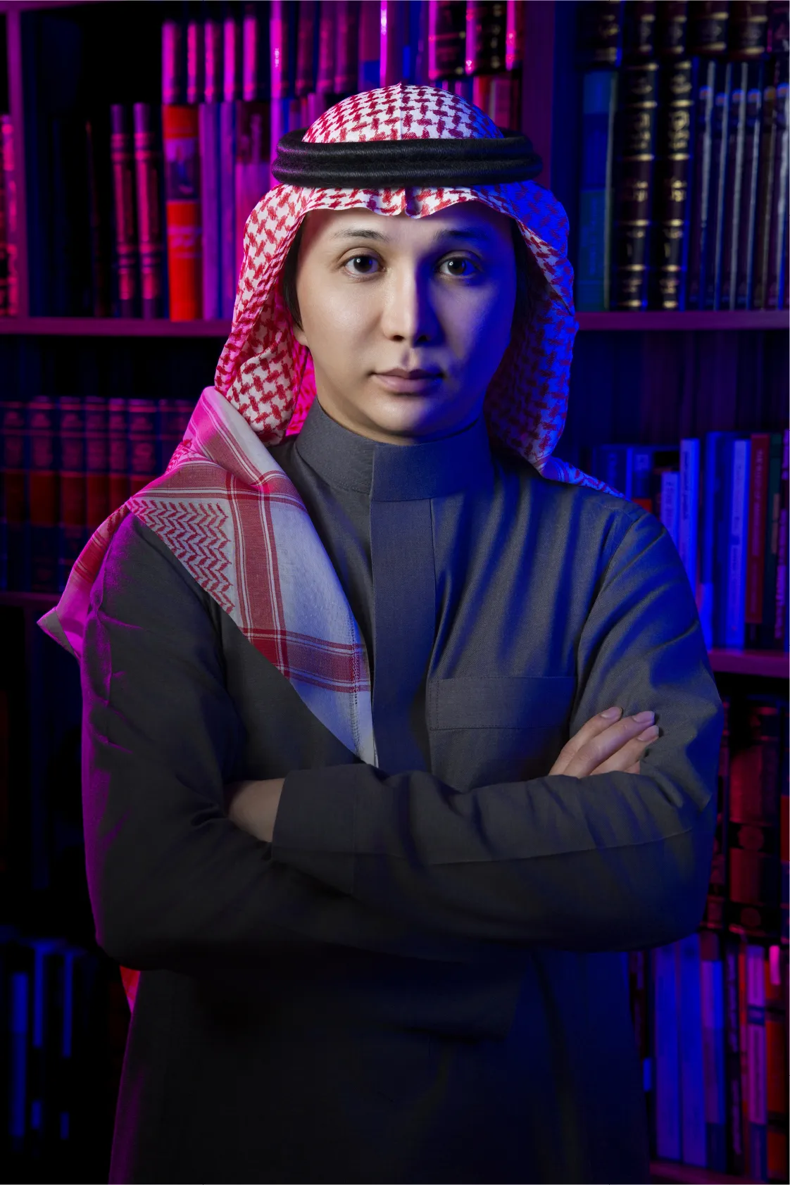 Portrait of a man wearing traditional Middle Eastern attire with a checkered headscarf and white thobe, arms crossed.