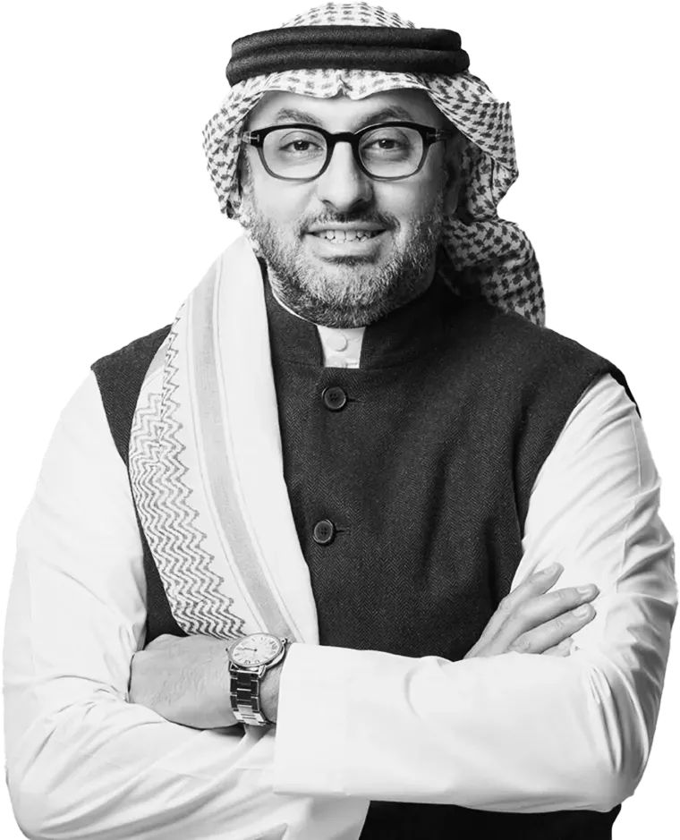 Smiling man wearing glasses, traditional Saudi headscarf, and dark vest with arms crossed.