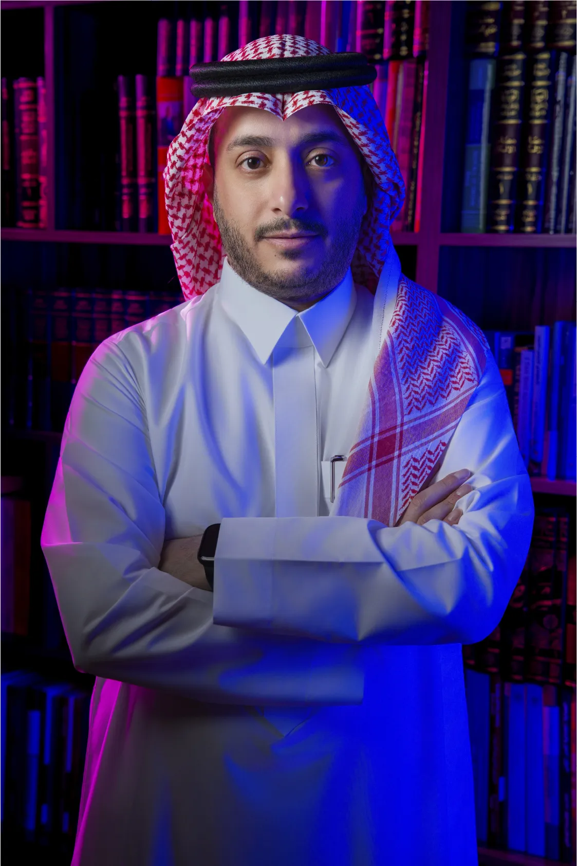 Portrait of a man wearing traditional Middle Eastern attire with arms crossed against a blue background.
