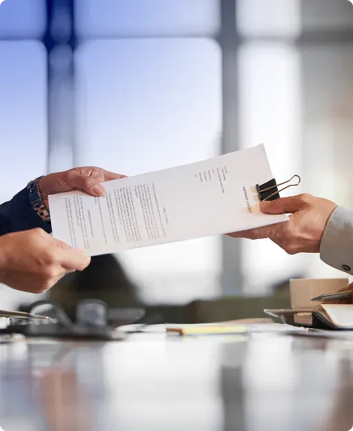 Two people exchanging a document with a binder clip in a professional office setting.