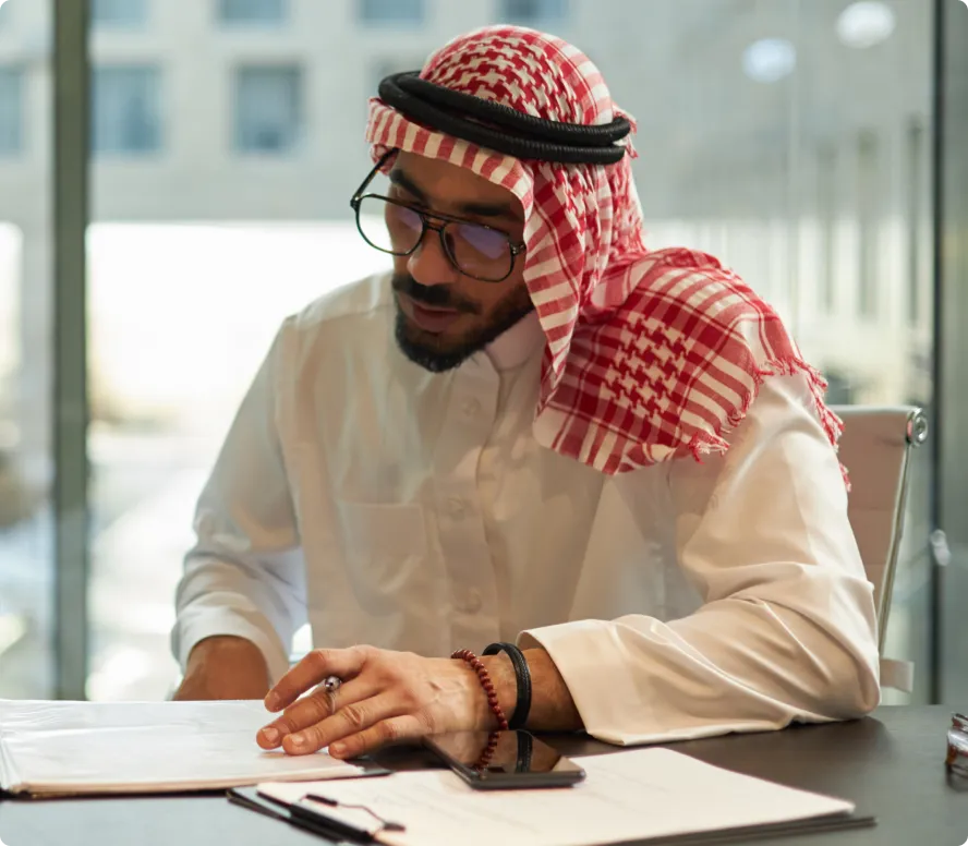 Person in suit holding a pen over a contract document on a clipboard near a laptop displaying graphs.