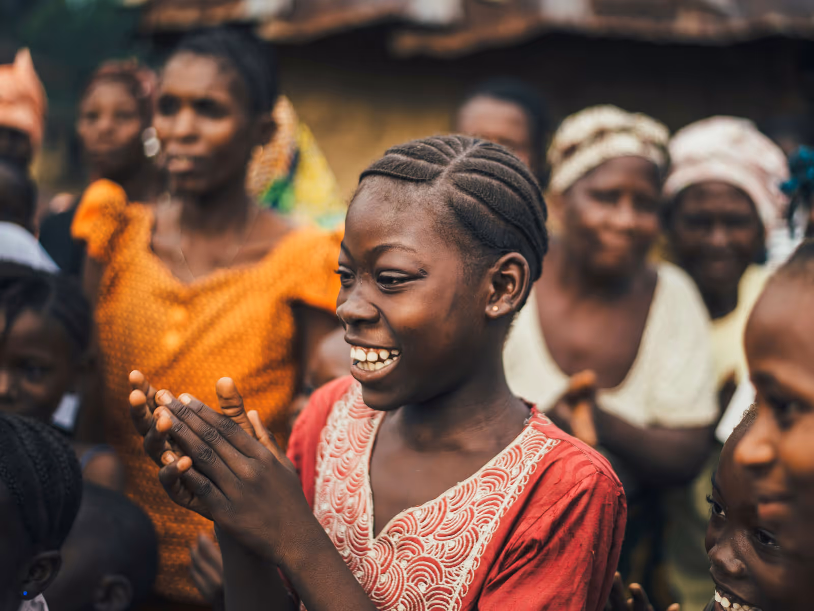 Smiling young girl clapping hands surrounded by a group of people in colorful clothing.