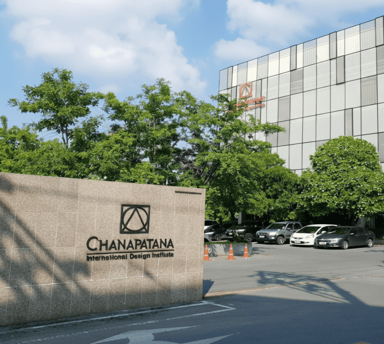 Exterior view of Chanapatana International Design Institute building with parked cars and green trees under a blue sky.