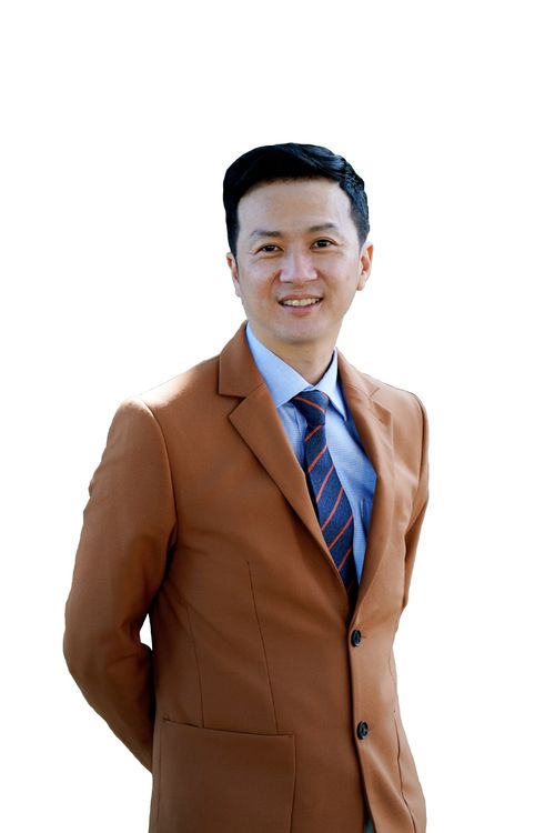 Smiling man wearing a brown suit jacket, light blue shirt, and striped tie against a white background.