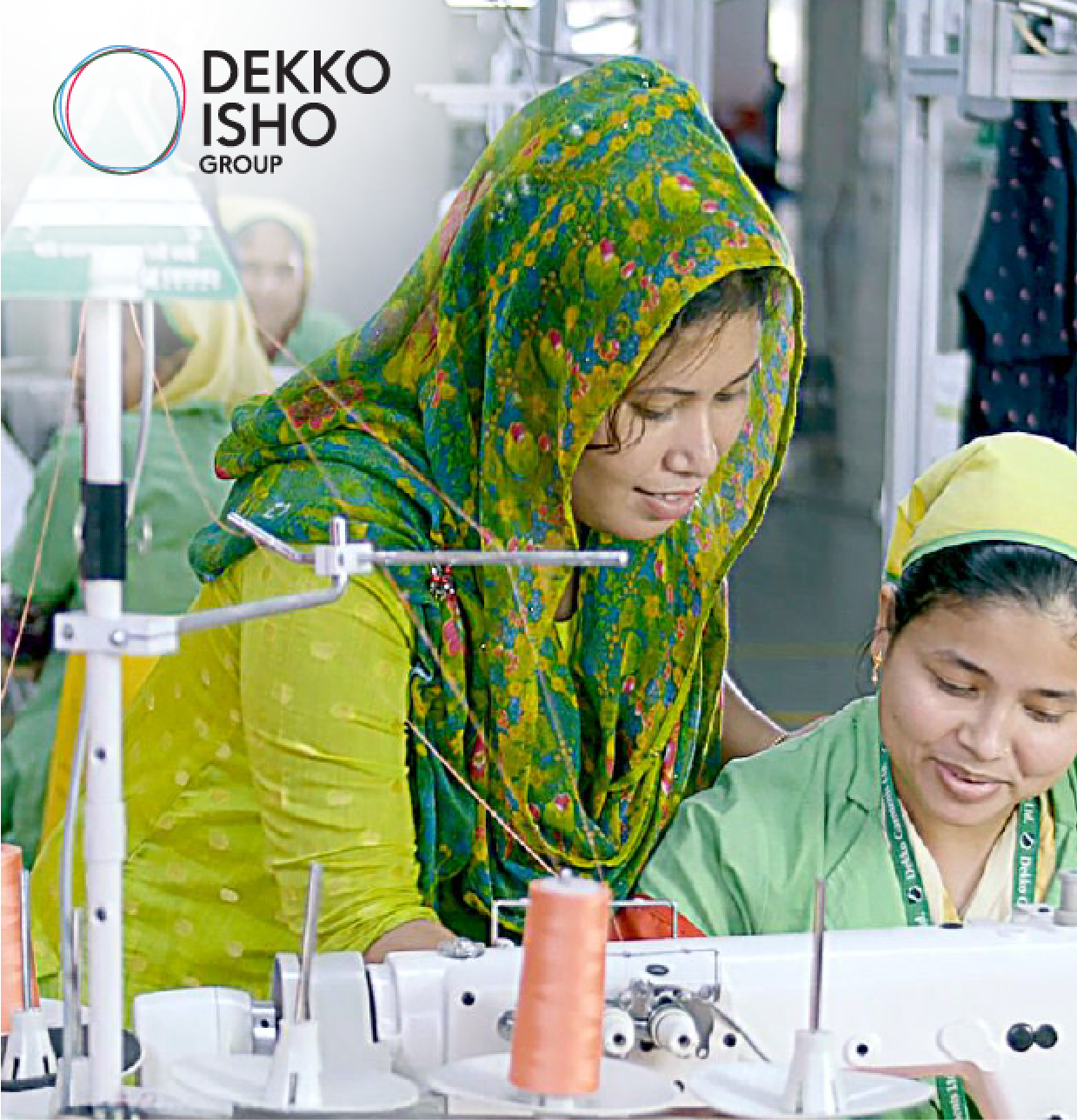 Two women working together at a sewing machine in a garment factory, one wearing a green floral scarf and the other in a yellow headscarf.