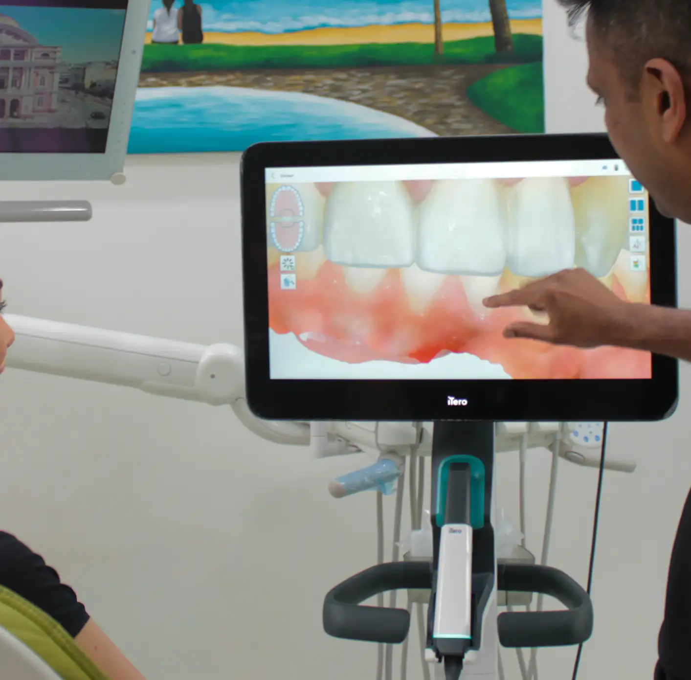 Dentist pointing at a digital 3D scan of upper teeth on a screen in a dental clinic.