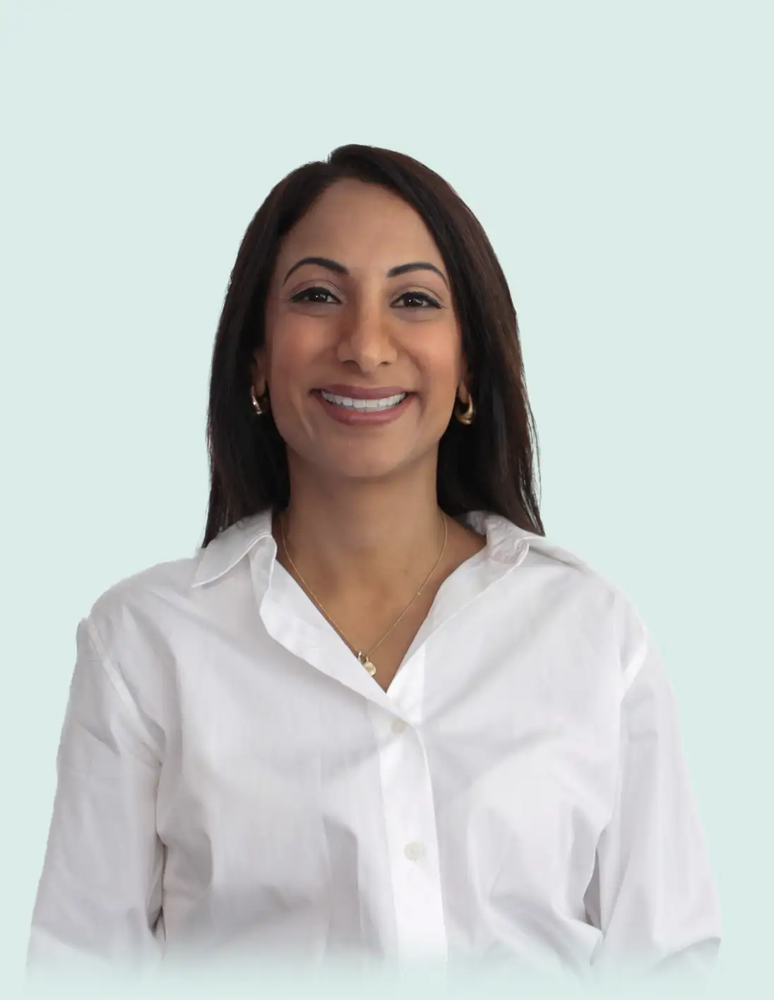 Smiling woman with long dark hair wearing a white button-up shirt and gold hoop earrings on a light blue background.