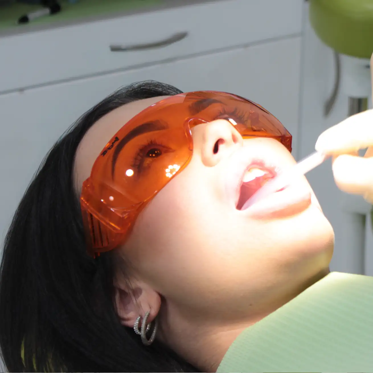 Woman wearing orange protective glasses having her teeth cleaned by a dental professional.