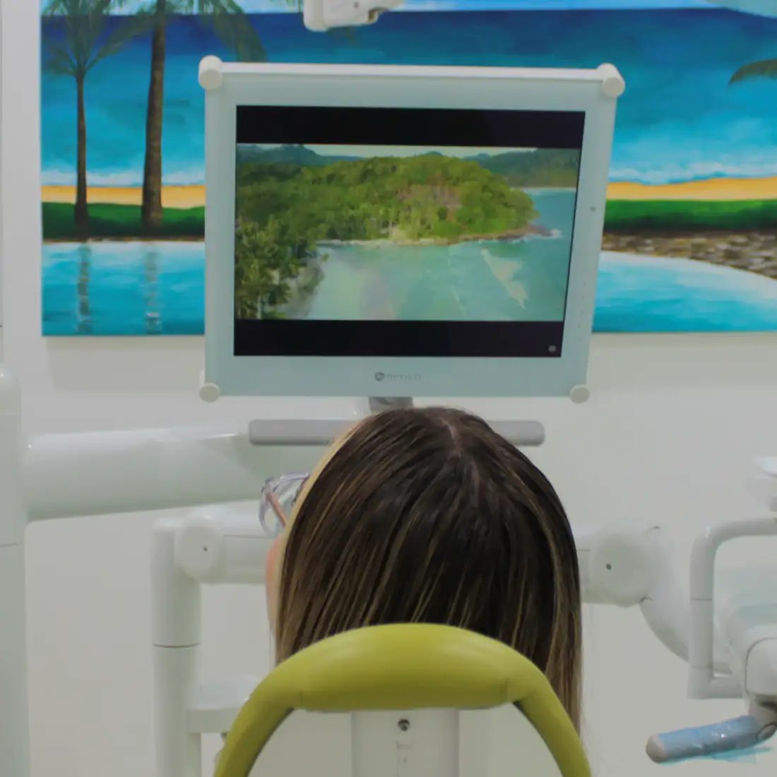 Person sitting in a dental chair looking at a monitor displaying an island landscape.