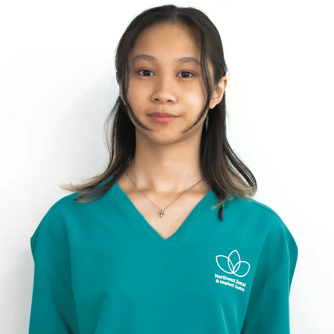 Young woman with long dark hair wearing a teal medical scrub top with Northwest Dental & Implant Centre logo.
