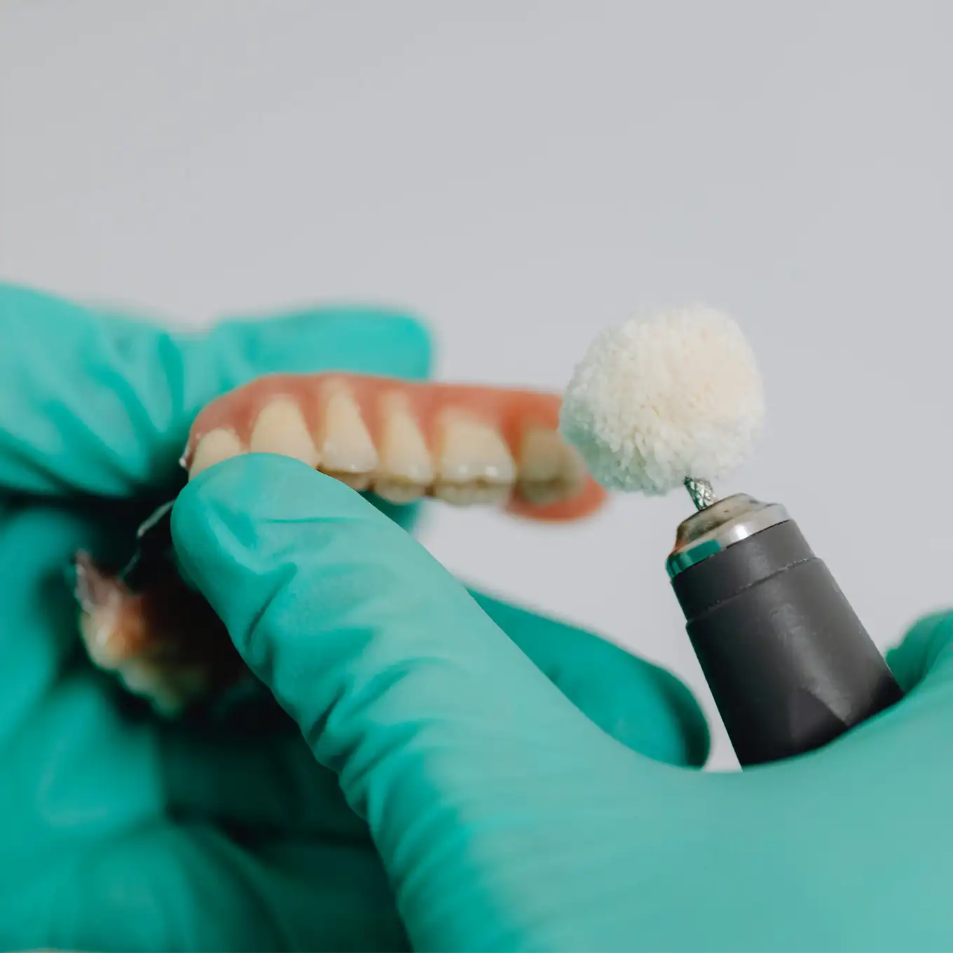 Gloved hands holding a dental tool polishing a set of dentures.