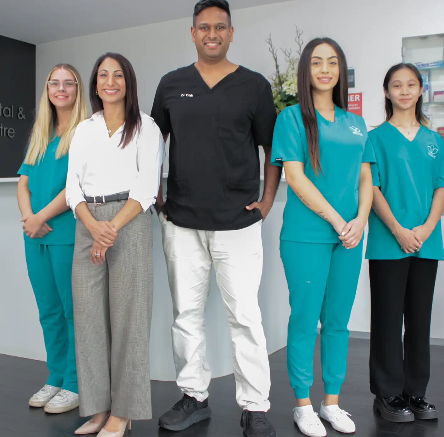 Five smiling dental professionals standing in a row inside a dental clinic.