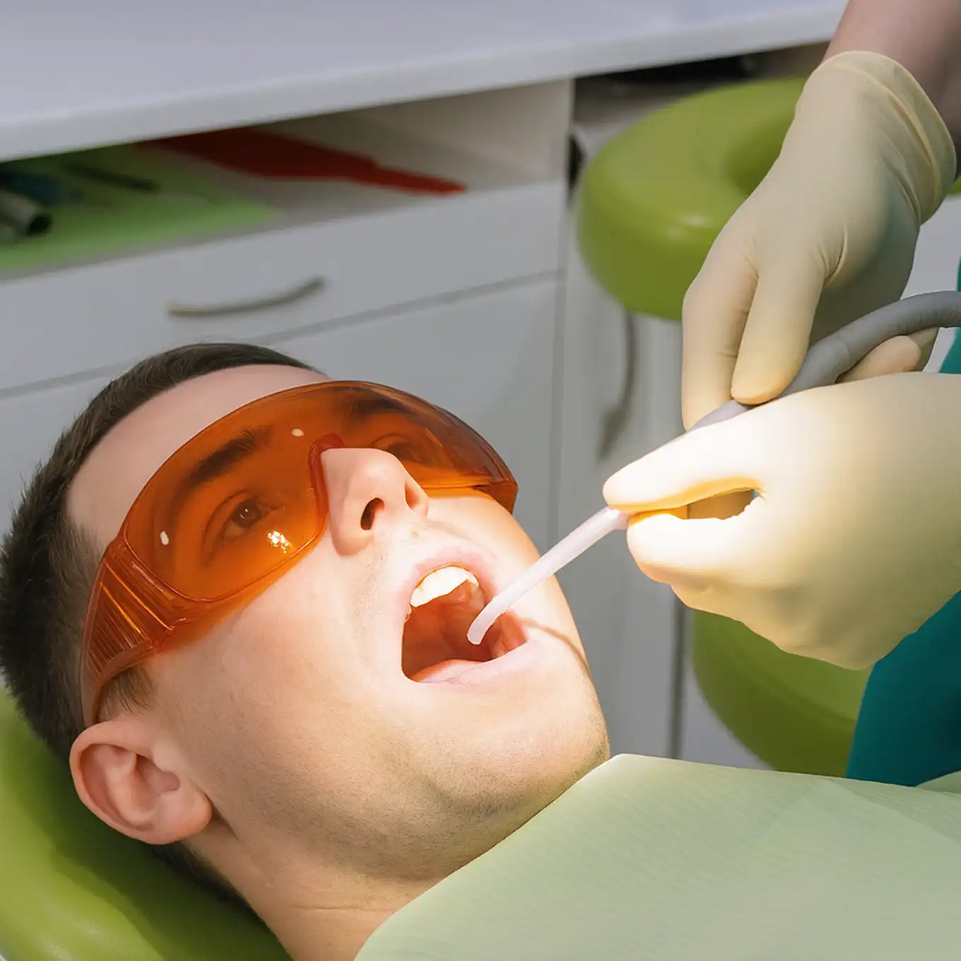 Patient wearing orange protective glasses receiving dental filling treatment with a suction device.