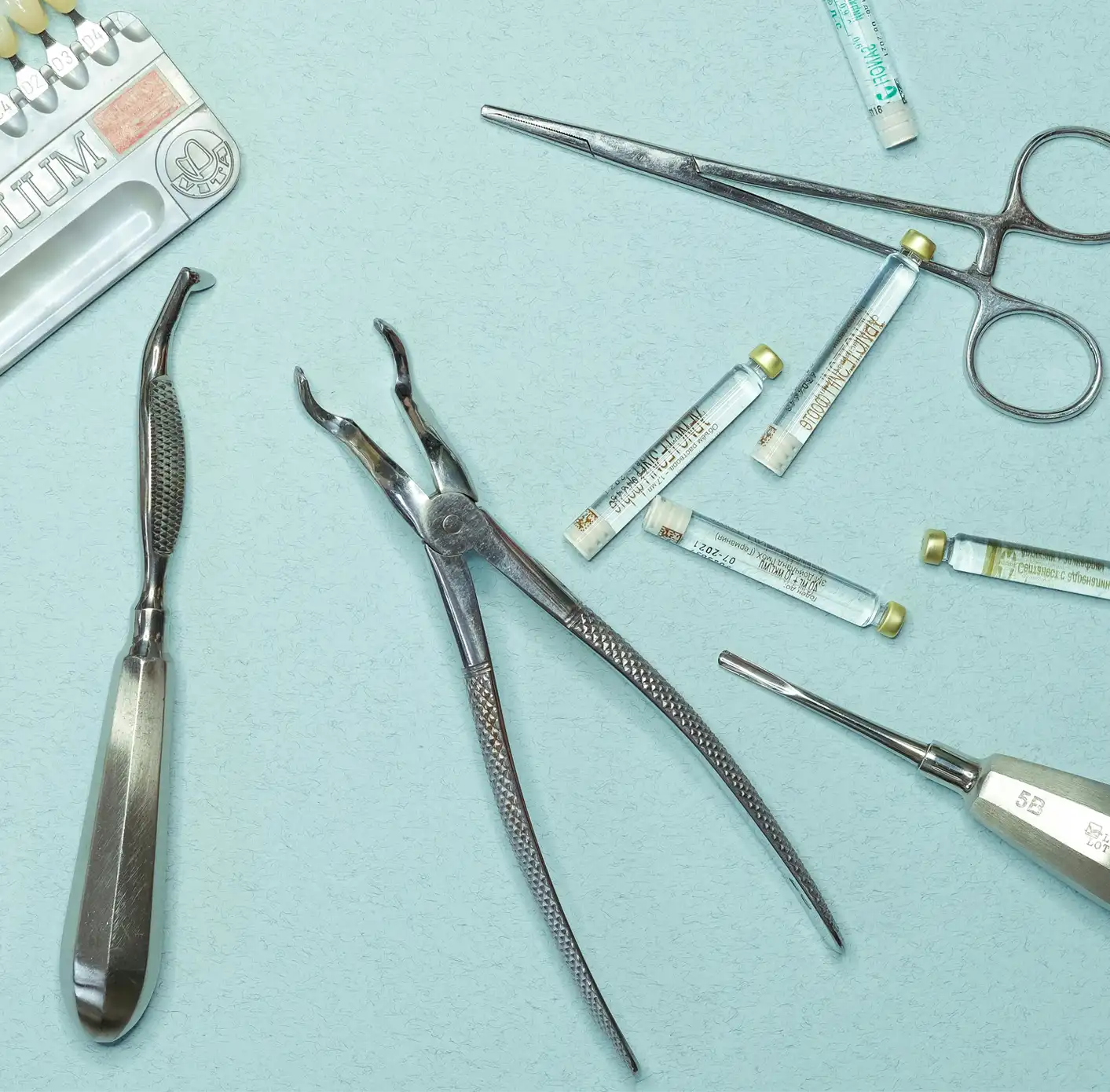 Various dental tools and small vials arranged on a light blue surface.