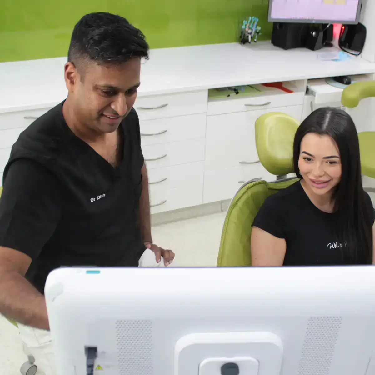 Dentist showing digital scan results to a female patient seated in a green dental chair.