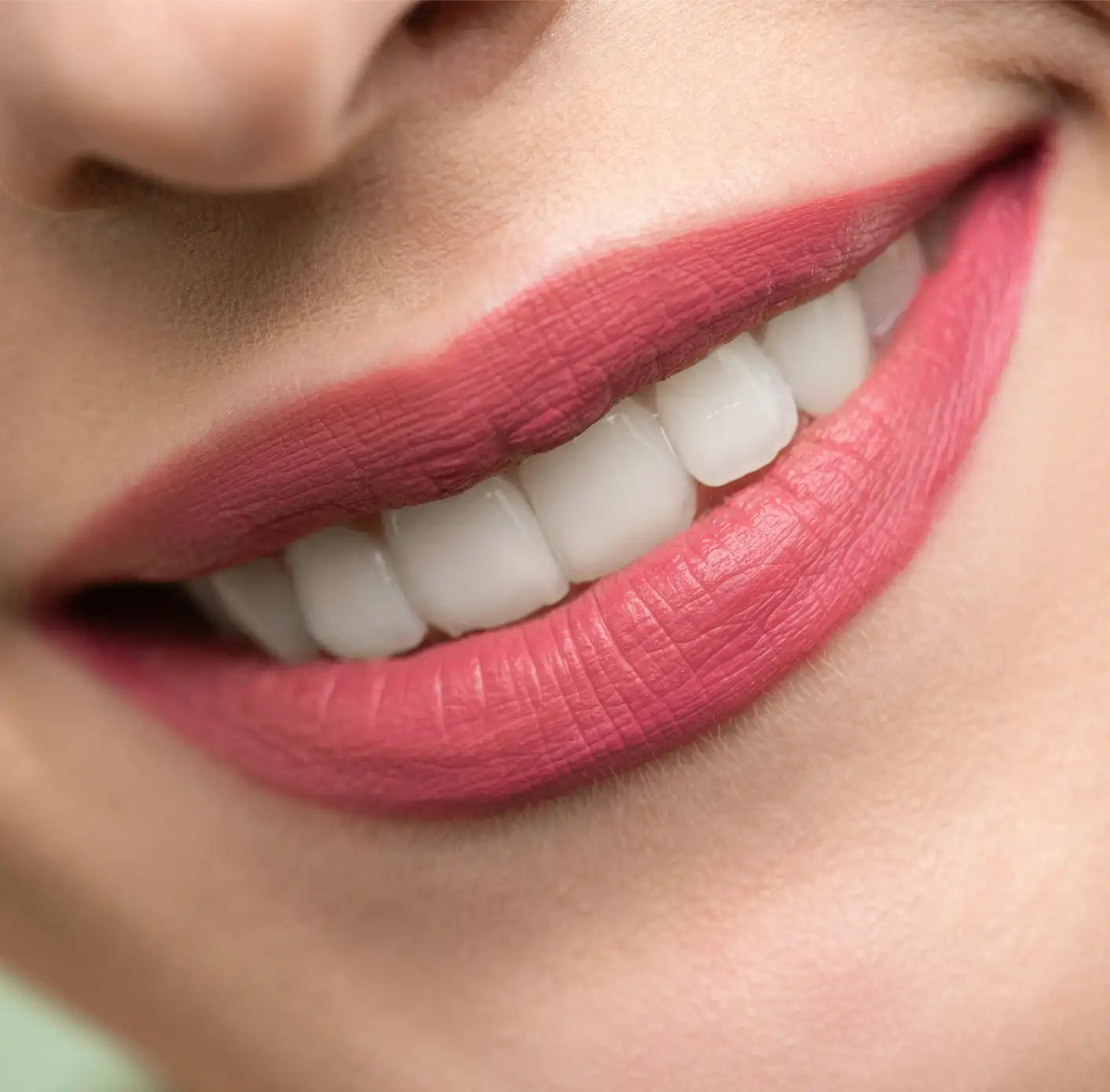 Close-up of a smiling mouth with smooth pink lipstick and white, straight teeth.