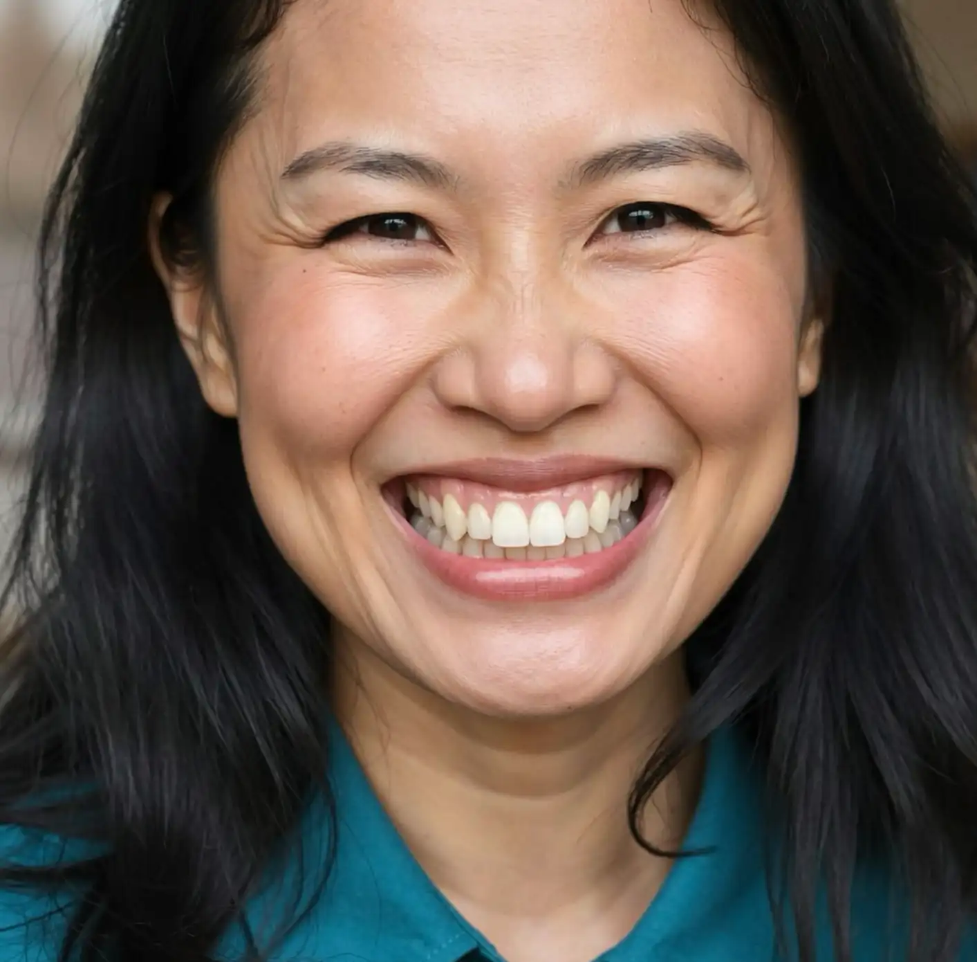 Close-up of a smiling woman with dark hair showing her whitened teeth.
