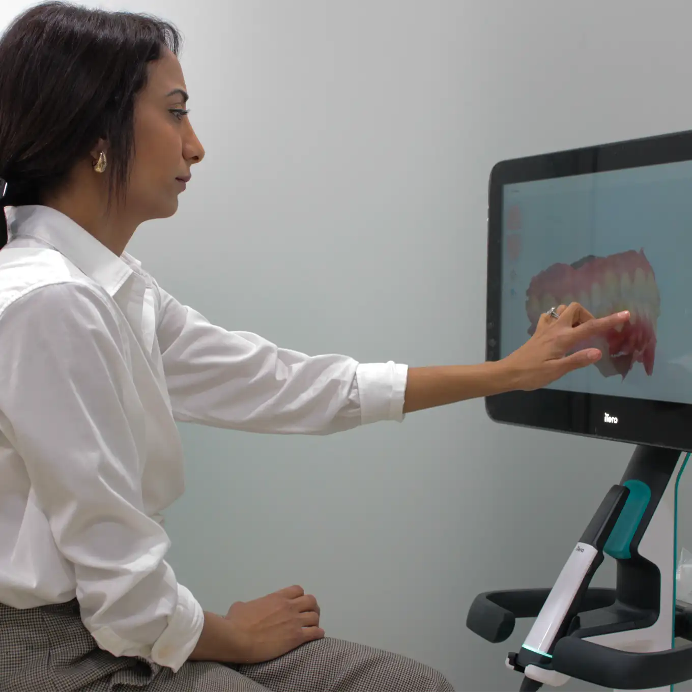 Woman in white shirt pointing at a 3D digital model of teeth on a screen.