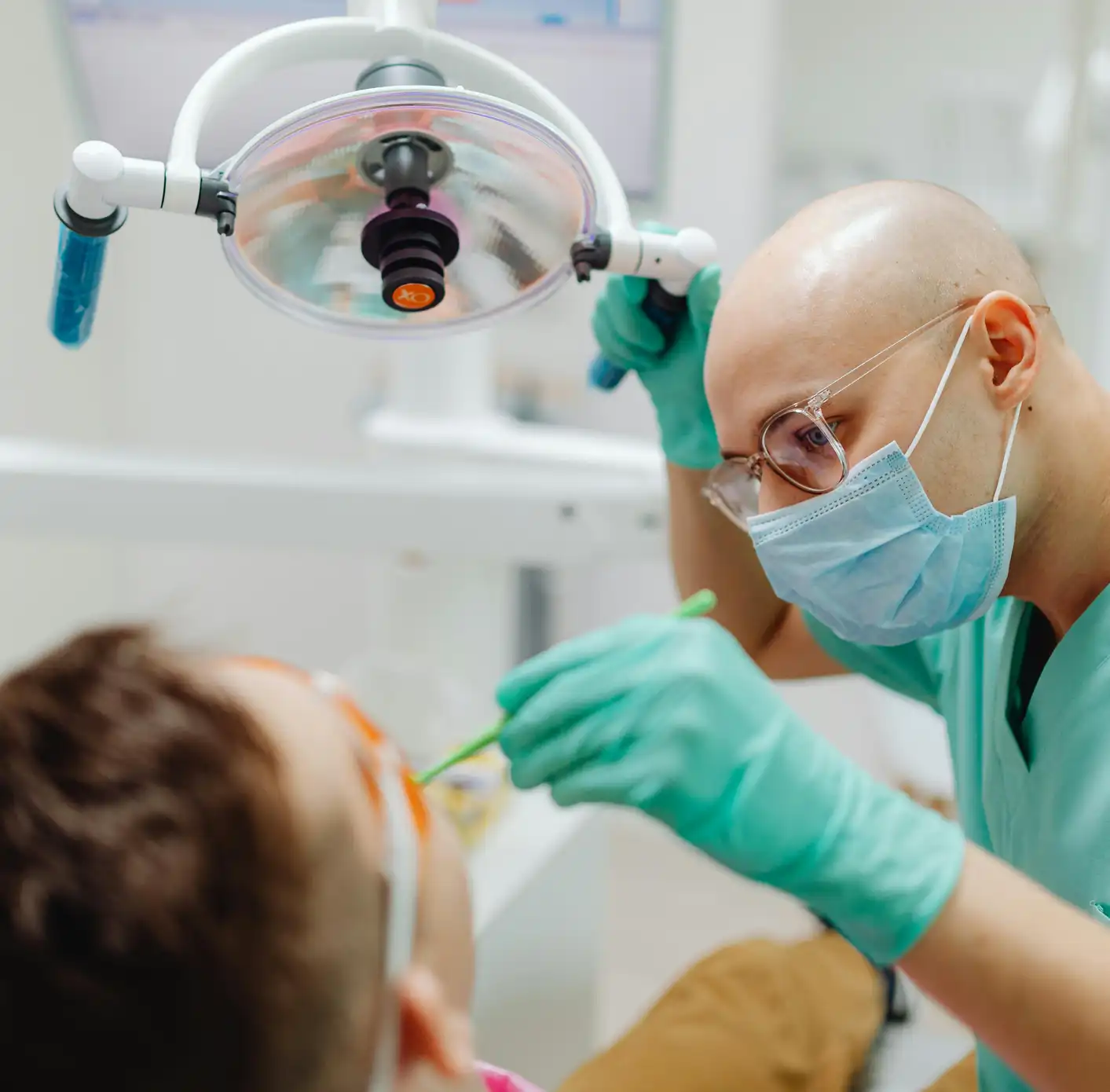 Dentist wearing a face mask and glasses performing dental treatment on a patient in a clinic.