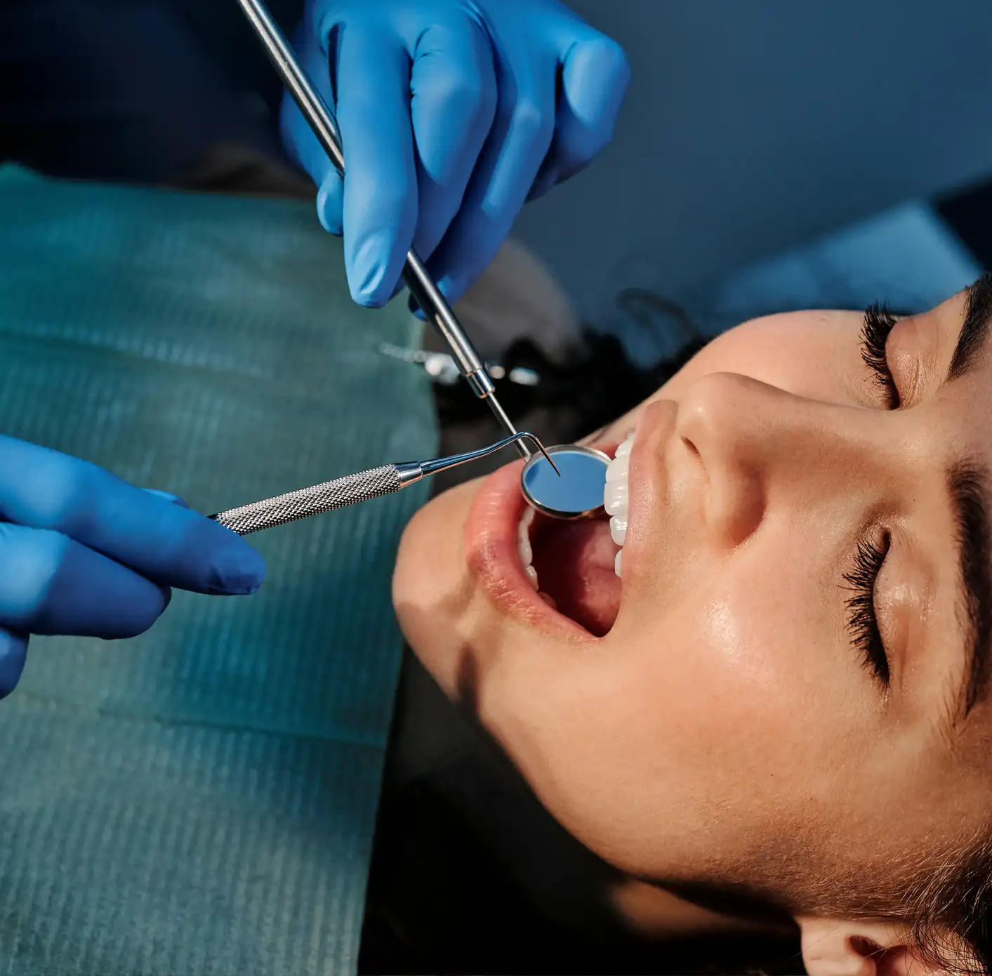 Close-up of a woman receiving a dental examination with a dental mirror and probe held by gloved hands.