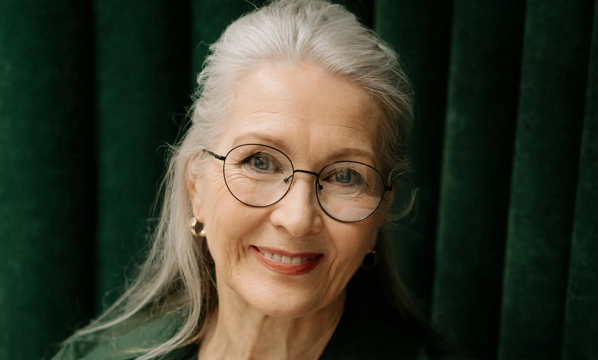 Smiling older woman with long silver hair smiling and showing her dental implants look natural.