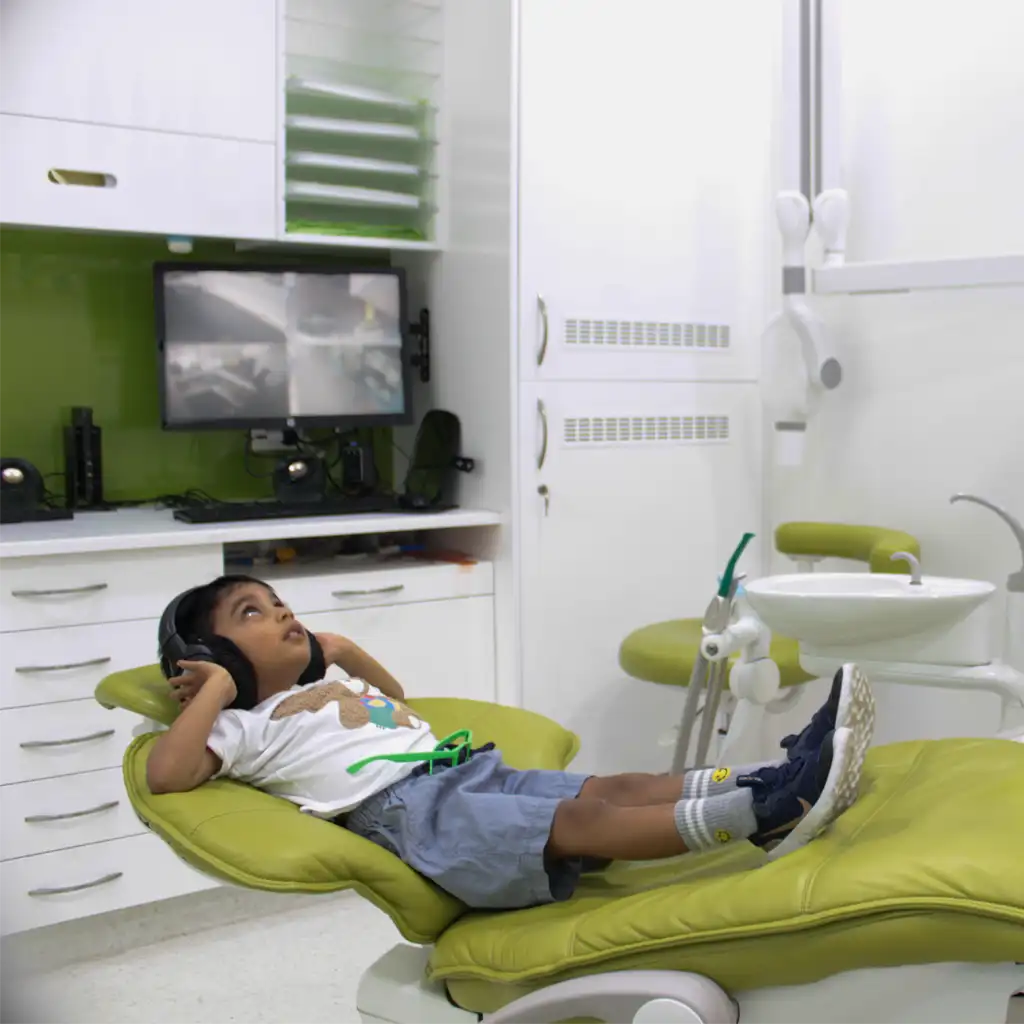 Young boy wearing headphones reclining on a green dental chair in a modern dental clinic.