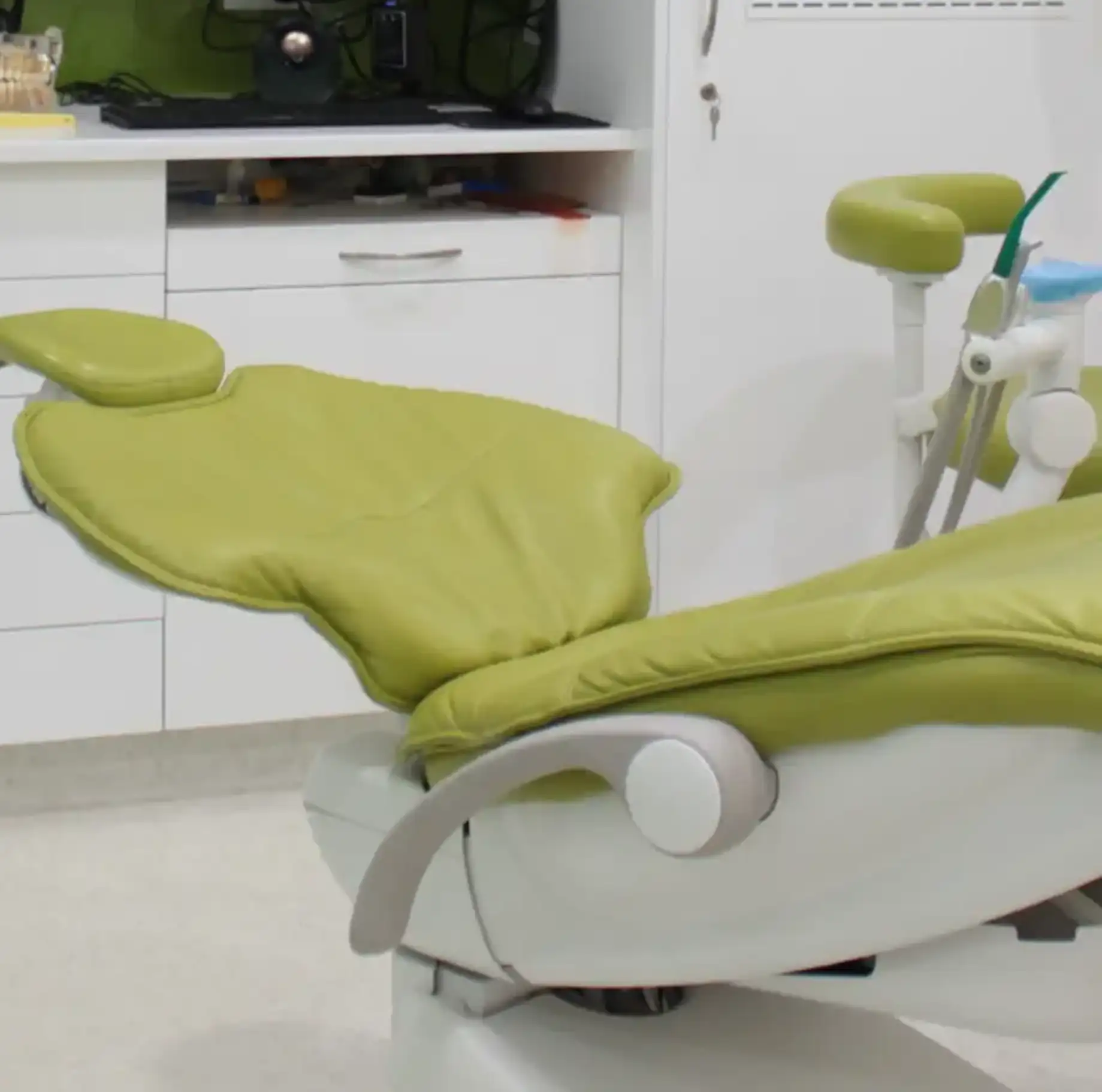Modern green dental chair in a clean, white dental clinic room.