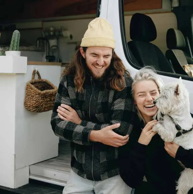 Smiling couple with a dog sitting by a van, sharing a joyful moment together.
