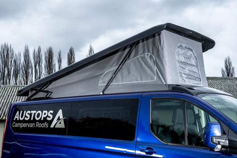 Blue campervan with raised grey pop-up roof and Austops Campervan Roofs logo on side.