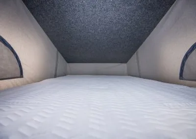 Inside view of a camper van bed with quilted mattress and fabric walls.