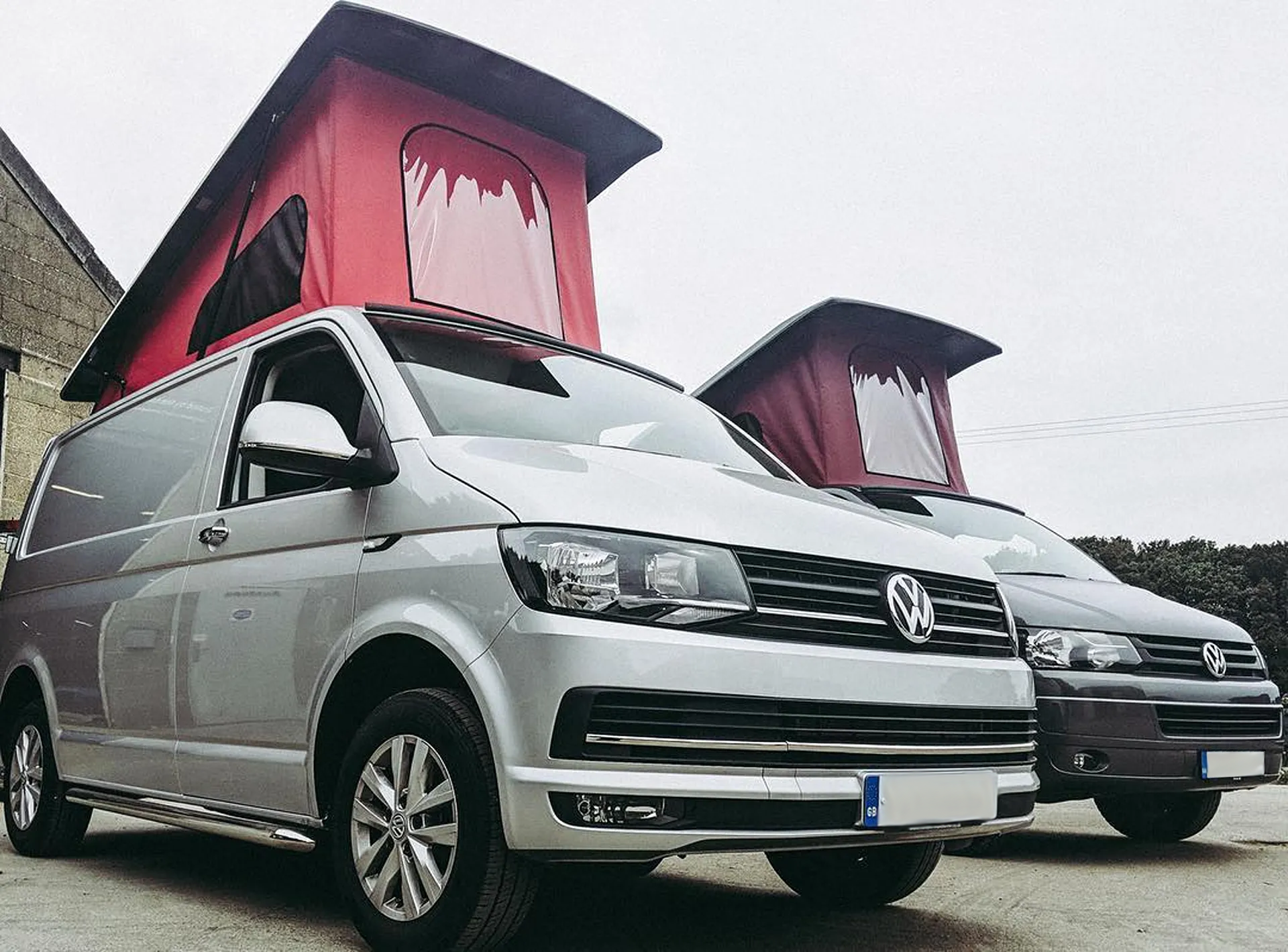 Two Volkswagen camper vans with raised red pop-up roofs parked side by side.