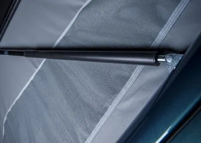 Close-up of a black cylindrical gas spring strut attached to a fabric surface and metal frame.