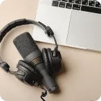Black microphone and headphones placed next to an open laptop on a beige surface.