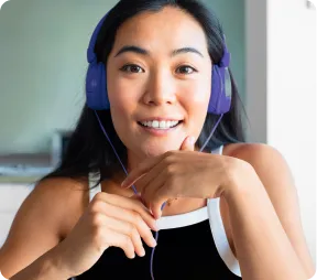 Smiling woman with long dark hair wearing purple headphones and a black sleeveless top.