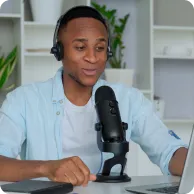 Man wearing headphones speaking into a microphone while working on a laptop.