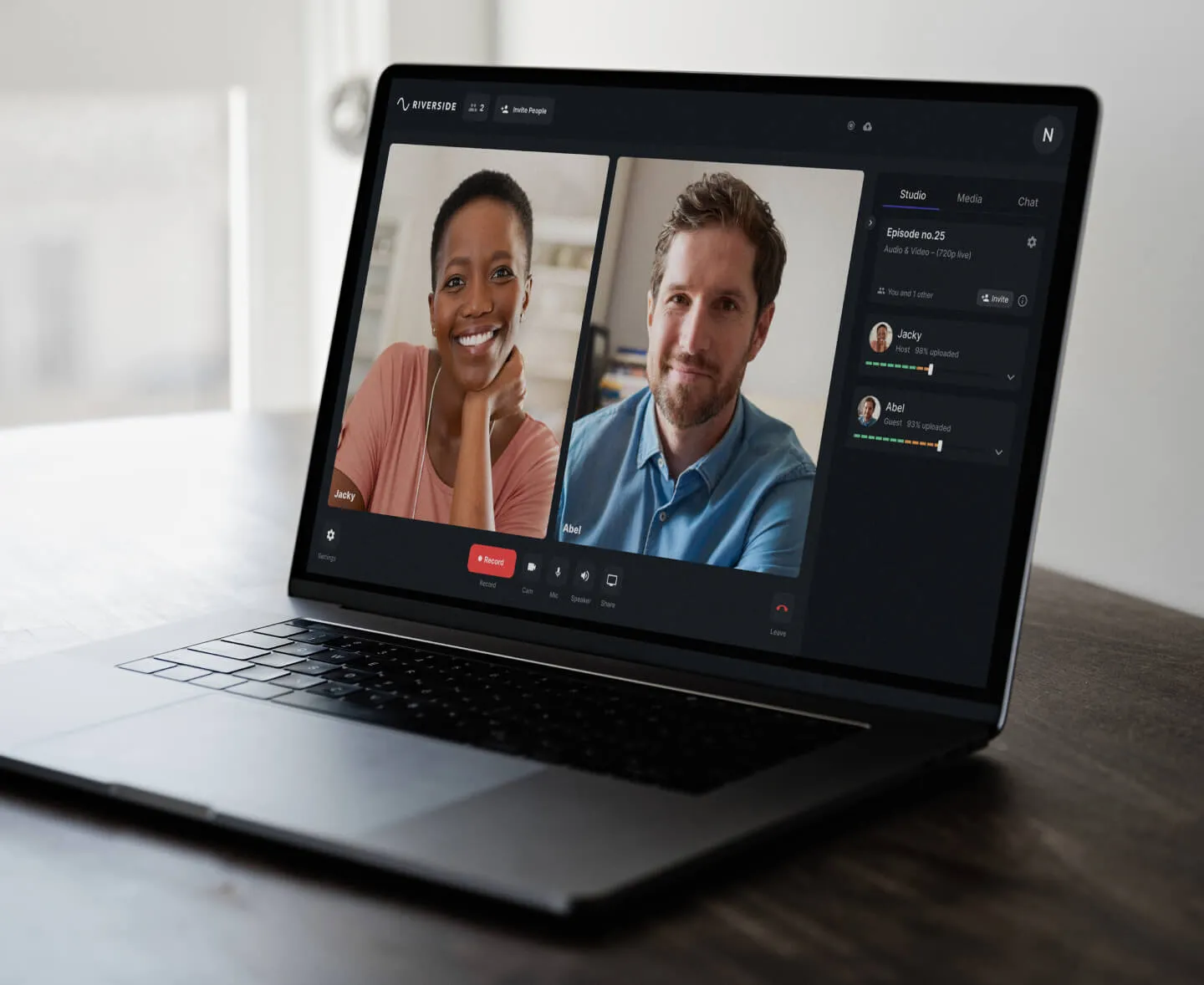 Open laptop on table showing a video call with two smiling people, a woman and a man, using Riverside software interface.