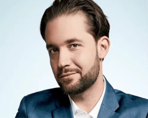 Man with short dark hair and beard wearing a blue suit and white shirt against a light background.
