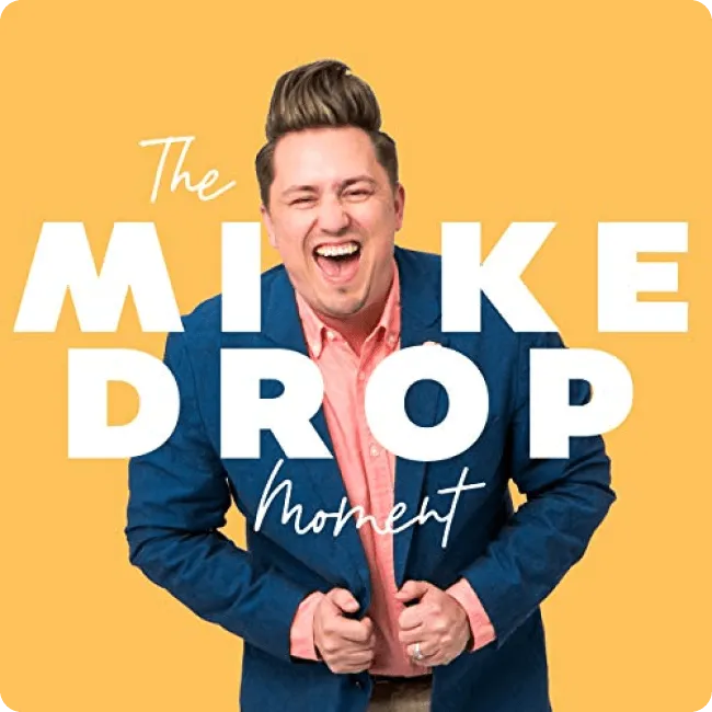 Man in a blue blazer and pink shirt laughing energetically against a yellow background with text 'The Mike Drop Moment'.