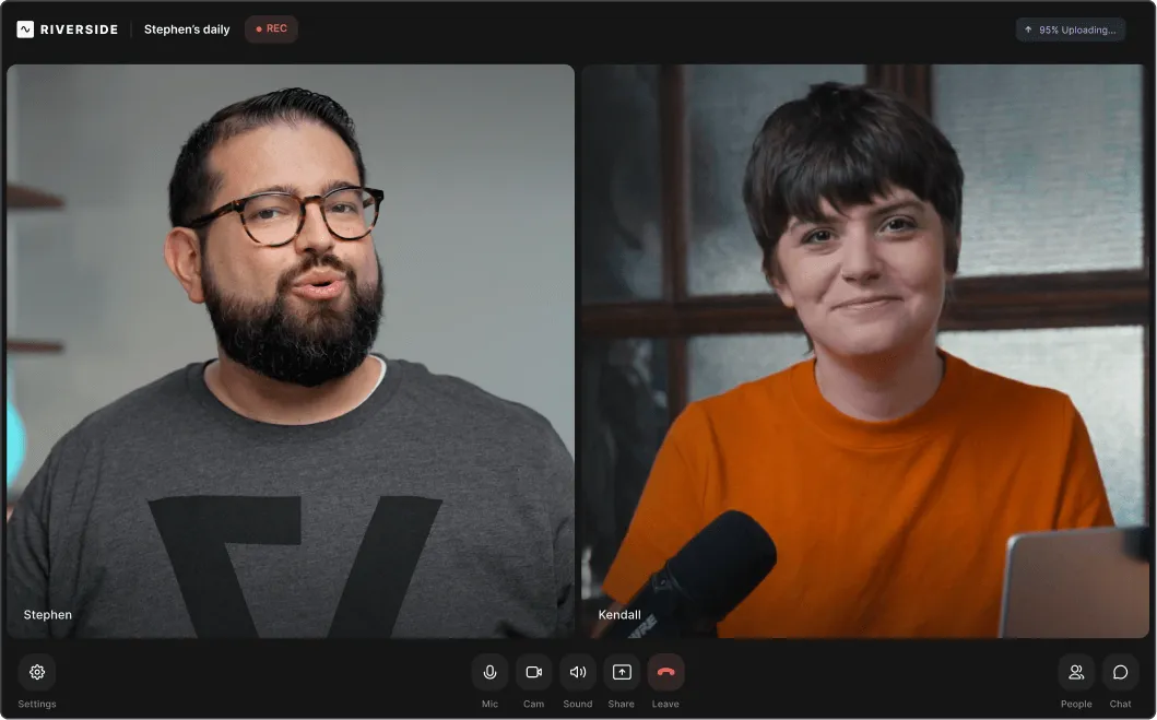 Video call screenshot showing two people: man with glasses and beard wearing a gray shirt labeled Stephen, and woman with short dark hair in an orange shirt labeled Kendall, speaking into a microphone.