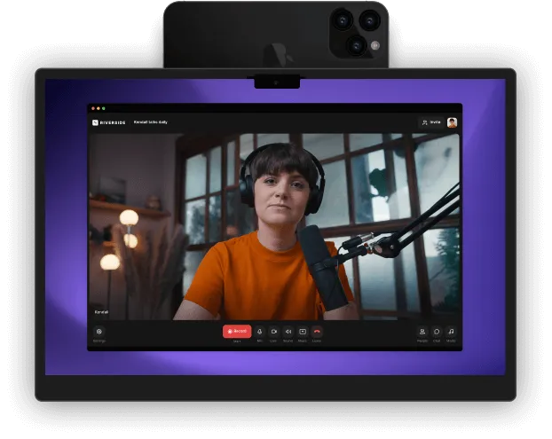 Tablet displaying a virtual meeting with a woman wearing headphones and speaking into a microphone, with a smartphone positioned behind it.
