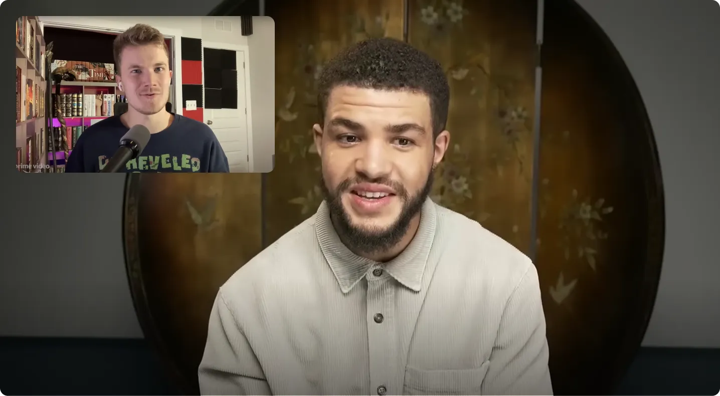 A man with short curly hair and a beard, wearing a light gray shirt, smiling and looking slightly to the side with a decorative circular screen behind him; an inset shows another man with short hair speaking into a microphone in a room with bookshelves.