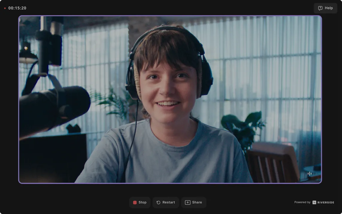 Smiling person wearing headphones and speaking into a microphone during a video recording session.