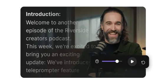 Man with long hair and beard smiling while speaking into a microphone, with teleprompter text visible on the left.