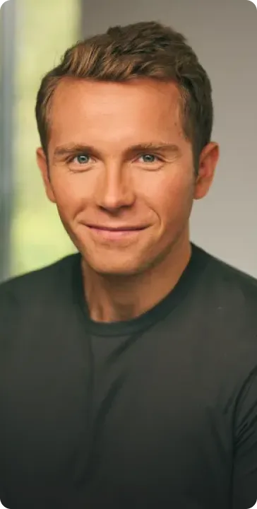 Smiling young man with short brown hair wearing a dark green shirt, posing indoors with a blurred background.