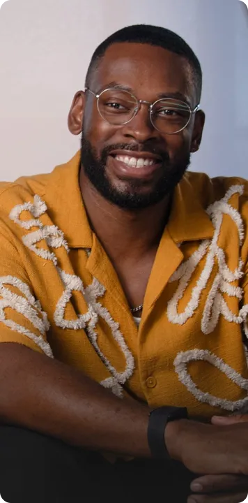 Smiling man with glasses and beard wearing a mustard yellow shirt with white patterns.