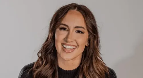 Smiling woman with long wavy brown hair against a light gray background.