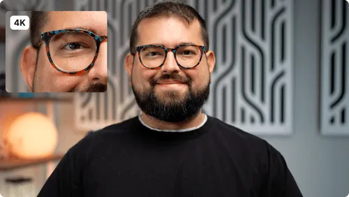 Smiling man with a beard wearing tortoiseshell glasses and a black shirt in front of a patterned gray wall.