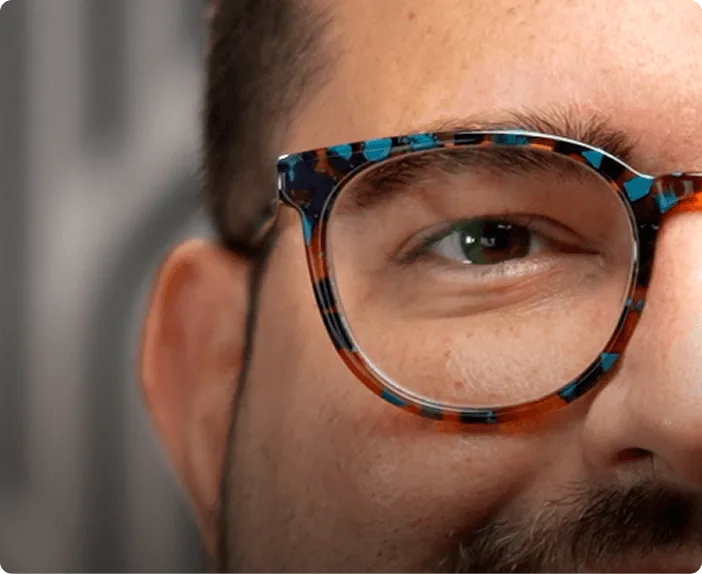 Close-up of a man's face focusing on his right eye wearing tortoiseshell glasses with blue and orange accents.