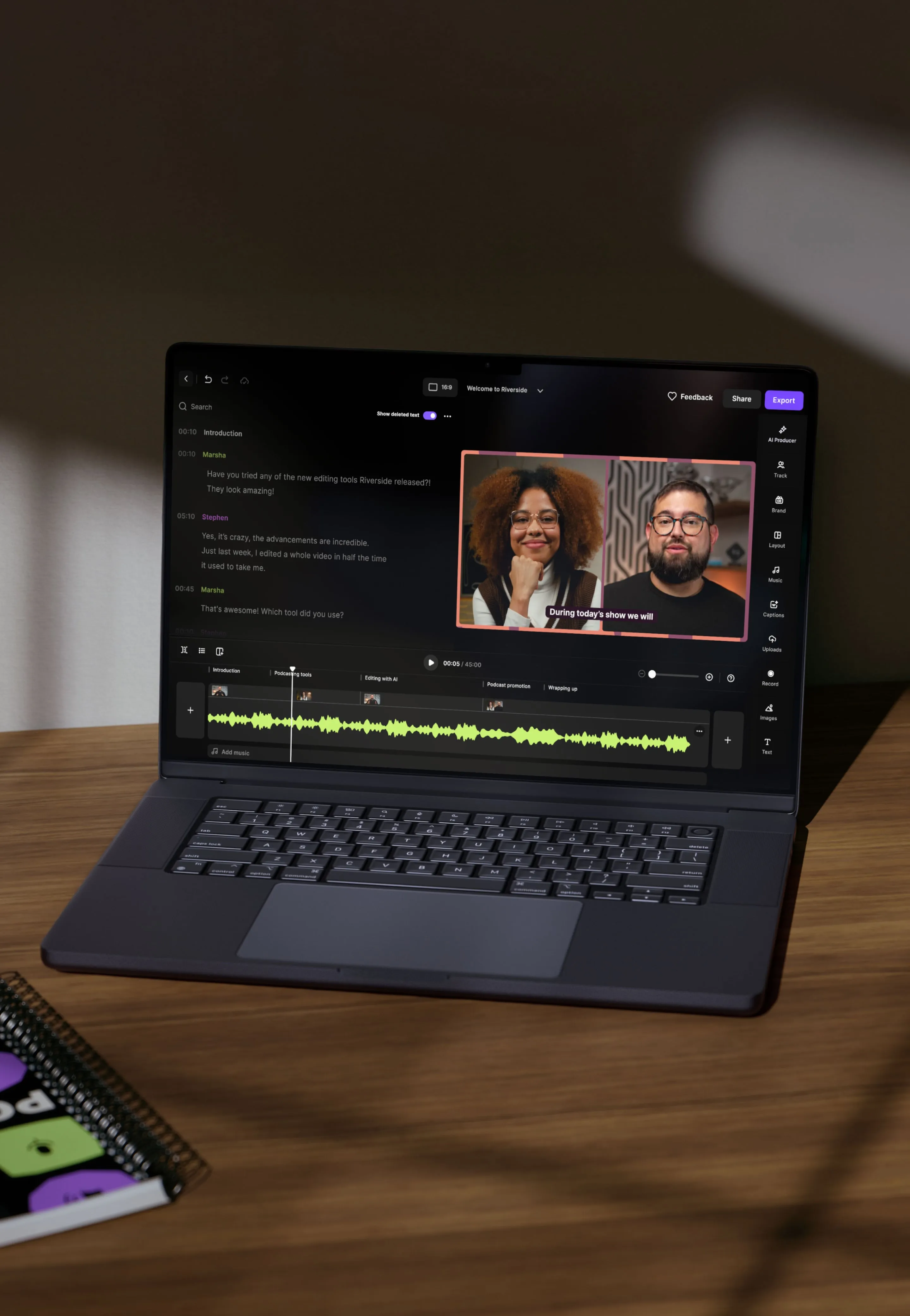 Open laptop on wooden desk displaying video editing software with audio waveforms, text editor, and two people in video thumbnails.